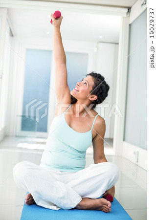 Pregnant woman lifting weight while sitting on exercise mat Pregnant woman lifting weight while sitting on exercise mat 19029737