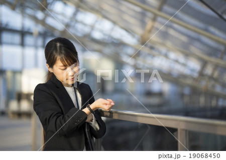 空港でアポイントがあり腕時計を見て約束の時間を気にするスーツ姿の若い会社員風女性CA乗務員 19068450