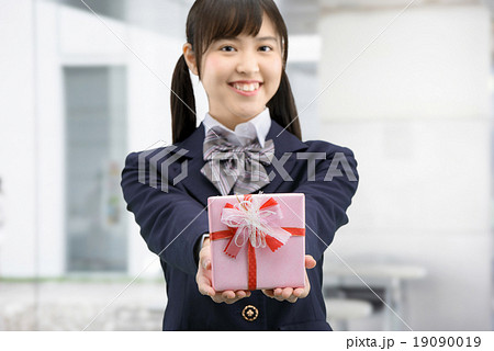プレゼントを抱えて立っている制服姿の女子高生のポーズの写真素材