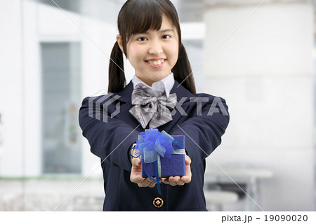 プレゼントを抱えて立っている制服姿の女子高生のポーズの写真素材