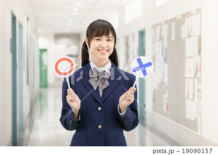 学校の廊下で○×サインを持って立っている制服姿の女子高生のポーズ 19090157