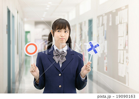 学校の廊下で○×サインを持って立っている制服姿の女子高生のポーズ 19090163