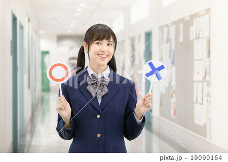 学校の廊下で○×サインを持って立っている制服姿の女子高生のポーズ 19090164