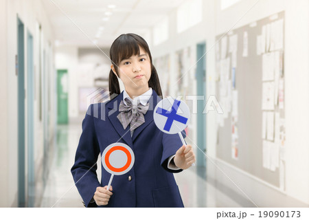 学校の廊下で○×サインを持って立っている制服姿の女子高生のポーズ 19090173