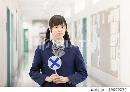 学校の廊下で○×サインを持って立っている制服姿の女子高生のポーズ 19090232