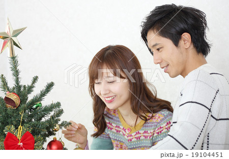 クリスマスツリーを飾るカップル 19104451
