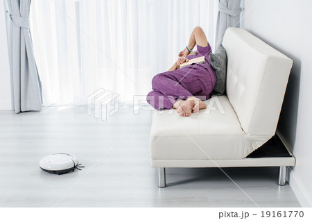 Senior woman reading a book while robot cleaning 19161770