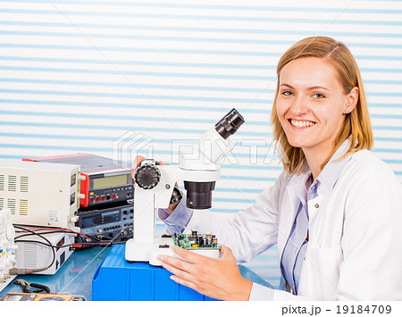 A young female researcher in a lab coat is peering into a micros 19184709