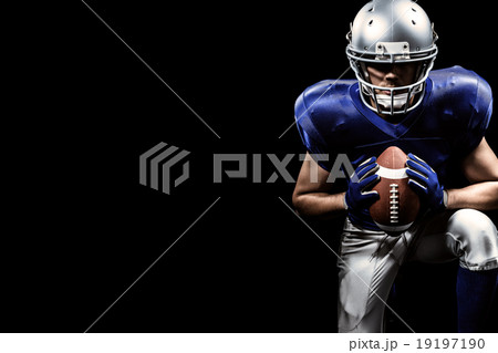 Composite image of determined american football player holding ball while kneeling 19197190
