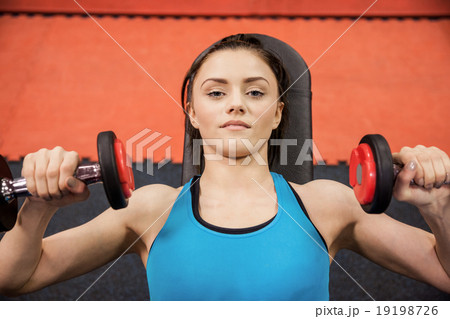Focused woman lifting dumbbells while lying down Focused woman lifting dumbbells while lying down 19198726