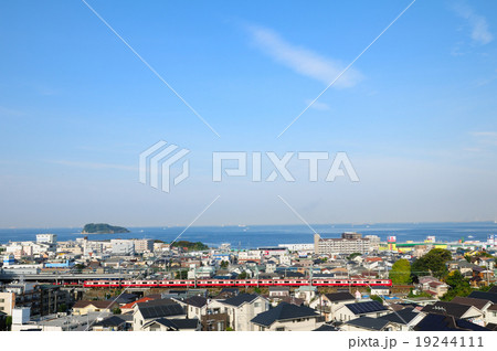 猿島を望む浦賀水道を背景に横須賀の住宅街を走る京急電車 19244111