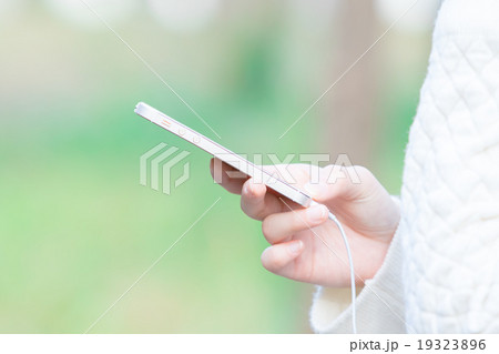 屋外で携帯電話で音楽を聴く女性　スマートフォン　スマホ　手元　パーツ 19323896