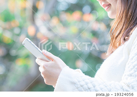 屋外で携帯電話で調べ物をする女性 検索 携帯をいじる スマートフォン スマホ 手元 パーツの写真素材