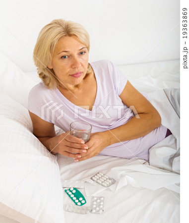 Sad mature woman laying in bed with pills 19363869