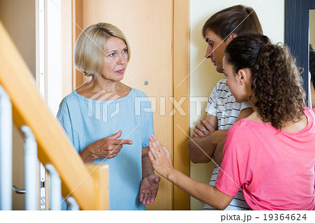 Young spouses receiving irritated senior neighbor at doorway Young spouses receiving irritated senior neighbor at doorway 19364624