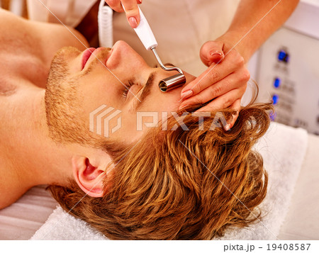 Young man receiving electric facial massage. 19408587