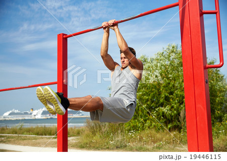 young man exercising on horizontal bar outdoors 19446115