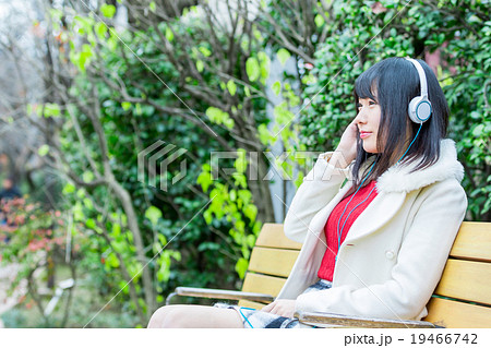 ミュージック ヘッドホン 音楽を聴く若い女性 女の人 黒髪 カジュアル 屋外の写真素材