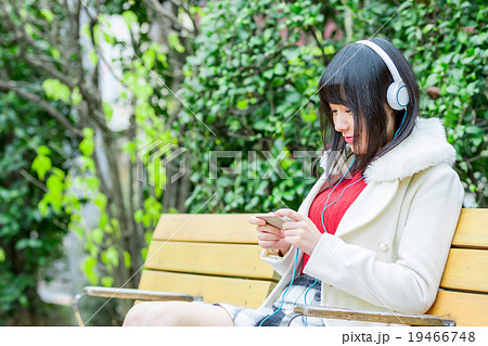 ミュージック ヘッドホン 動画を観る女性 音楽を聴く若い女性 女の人 黒髪 カジュアル 屋外の写真素材