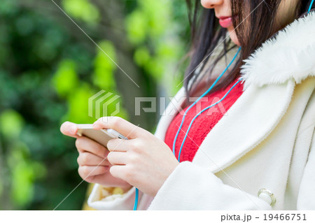 ミュージック　ヘッドホン　動画を観る女性　音楽を聴く若い女性　女の人　黒髪　カジュアル　屋外 19466751