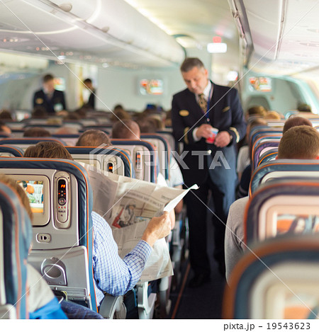 Steward and passengers on commercial airplane. 19543623