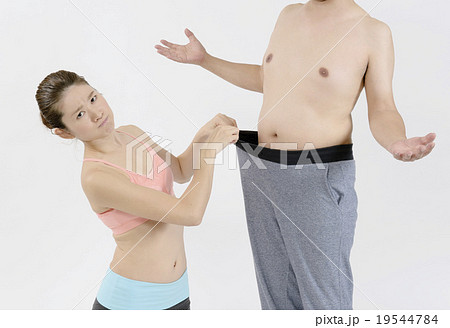 太った男性のお腹の前で怒った顔のスリムな女性の写真素材
