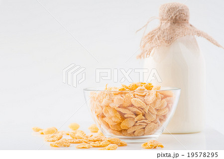 Milk and bowlful of corn flakes on white surface. Milk and bowlful of corn flakes on white surface. 19578295