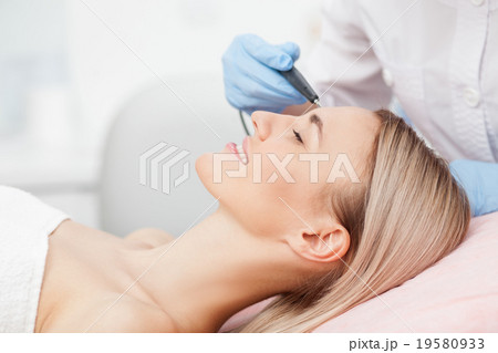 Skillful young cosmetologist is treating her 19580933