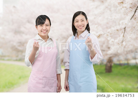 満開の桜並木に立っているエプロン姿の2人の若い女性ホームヘルパー 19634753
