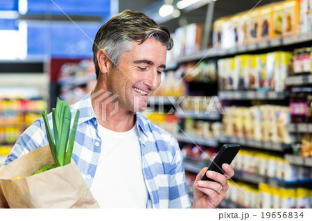 Smiling man with grocery bag using smartphone 19656834