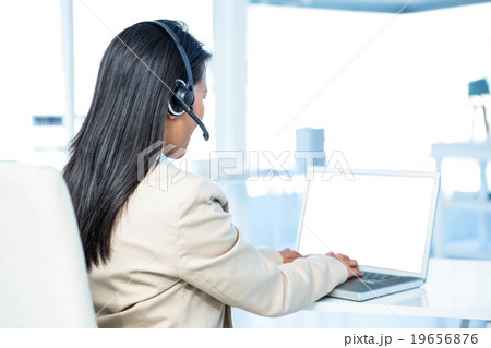 Smiling  businesswoman with headset using laptop  19656876