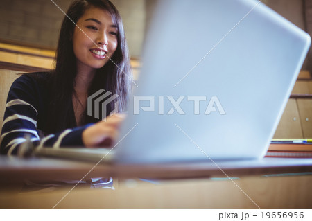 Happy student in lecture hall using laptop 19656956