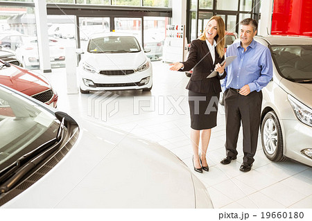 Smiling businesswoman showing car to customer Smiling businesswoman showing car to customer 19660180