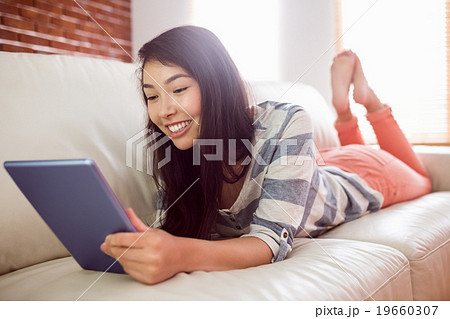 Smiling asian woman on couch using tablet Smiling asian woman on couch using tablet 19660307