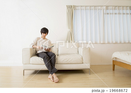 ソファーに座り読書をする若い男性の写真素材