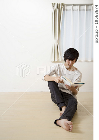 床に座り読書をする若い男性の写真素材
