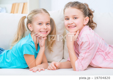 Cheerful little sisters sitting on the sofa Cheerful little sisters sitting on the sofa 19704820