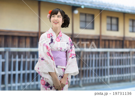 浴衣を着て古い家並みの前に立っている若い女性 19731136
