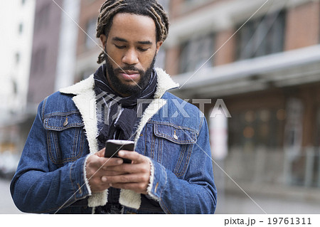 Serious man with dreadlocks using smart phone in street 19761311
