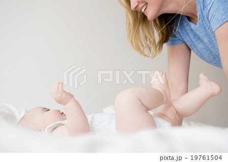 Baby girl (12-17 months) lying down on bed and mother leaning over Baby girl (12-17 months) lying down on bed and mother leaning over 19761504