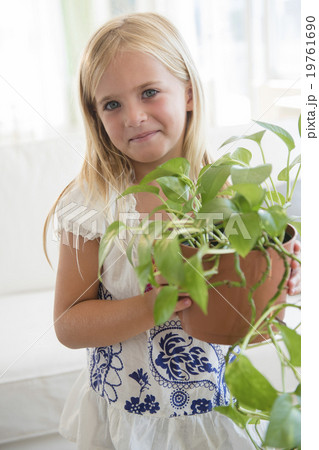 Girl (6-7) holding flower in flower pot 19761690