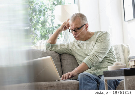 Man sitting on sofa using laptop at home Man sitting on sofa using laptop at home 19761813