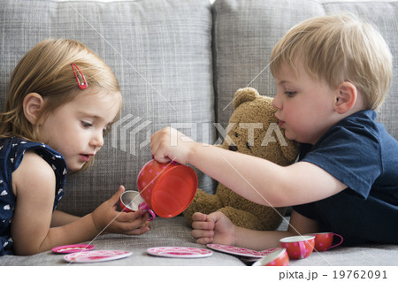Brother (2-3) and sister (2-3) having tea party with teddy bear 19762091