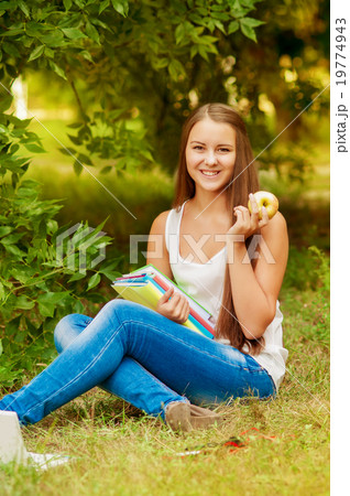 student with books on the grass eating an apple student with books on the grass eating an apple 19774943