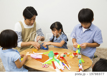 保育士の男性と折り紙をする子供たち 19786977