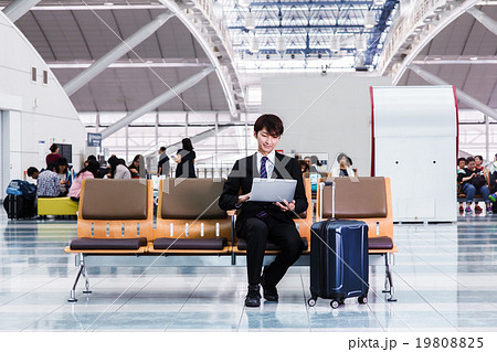 空港のロビーでパソコンをチェックするビジネスマン 空港のロビーでパソコンをチェックするビジネスマン 19808825
