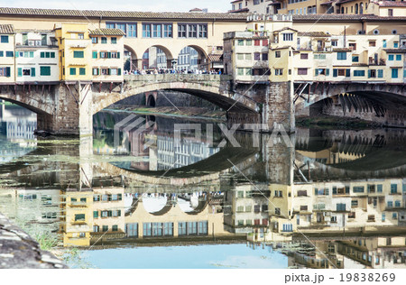Ponte Vecchio is mirrored in the river Arno, Florence, Italy, cu 19838269