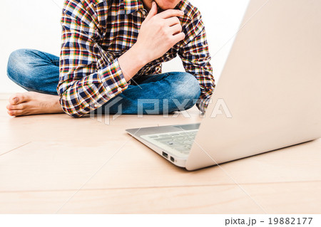 部屋の床でノートパソコンを操作している男性の写真素材