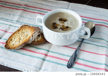 Bowl of mushroom soup with bread on wooden board 19898341