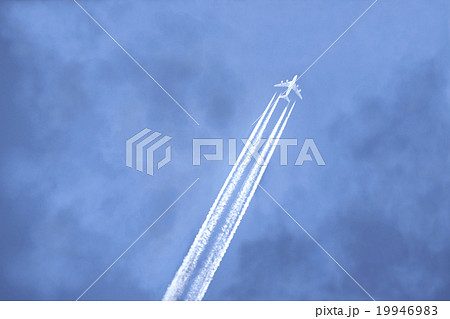 飛行機雲を噴射しながら雨雲を突き抜ける航空機の写真素材